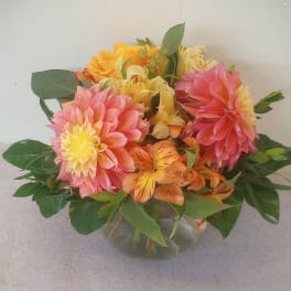 Mixed pink, yellow, and orange flowers arranged in a clear glass vase