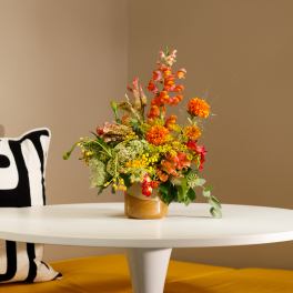 Colorful mixed flower arrangement in a gold vase on a white table