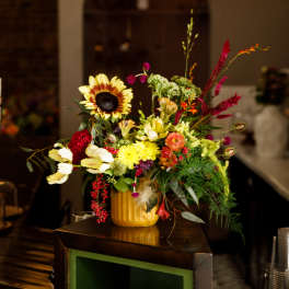 Colorful mixed flower arrangement in a yellow vase on a counter