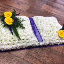 White floral casket spray with yellow flowers and purple ribbon