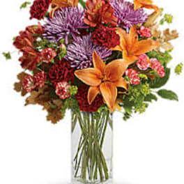Mixed bouquet of orange lilies, purple chrysanthemums, and red flowers in a clear glass vase