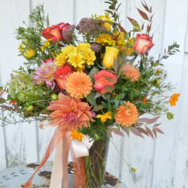 Mixed bouquet of roses, dahlias, and yellow blooms in a glass vase