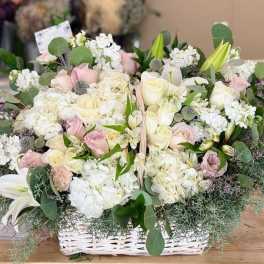 Basket arrangement of white and blush roses with lilies and greenery