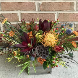 Mixed floral arrangement in a wooden box with orange and burgundy blooms
