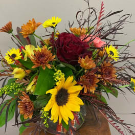 Mixed bouquet with a red rose, sunflowers, and orange daisies in a glass vase