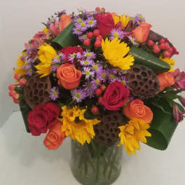 Mixed bouquet of roses, sunflowers, and purple daisies in a glass vase