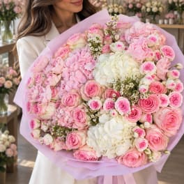 Woman holding a large bouquet of pink and white flowers wrapped in lavender paper