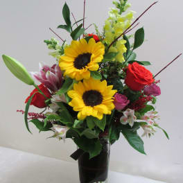 Mixed bouquet with sunflowers, roses, lilies, and snapdragons in a tall vase