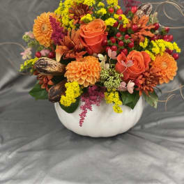 Orange and yellow floral arrangement in a white pumpkin-shaped container