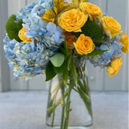 Bouquet of blue hydrangeas and yellow roses in a clear glass vase