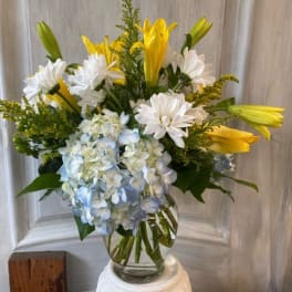 Yellow lilies and white daisies with blue hydrangea in a glass vase