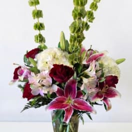 Mixed bouquet of lilies, hydrangeas, and red blooms in a glass vase