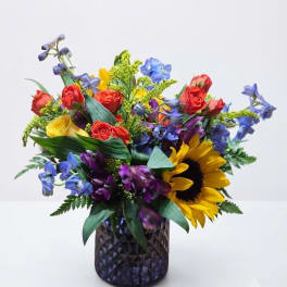 Colorful bouquet with roses, sunflowers, and blue flowers in a dark glass vase