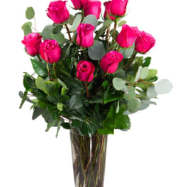 Tall arrangement of bright pink roses with lush foliage in a clear glass vase