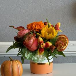 Autumn bouquet in a peach vase with a small decorative pumpkin beside it.