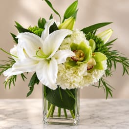 White lilies and pale green orchids in a clear glass vase