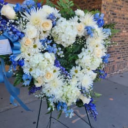 Heart-shaped floral wreath with white and blue flowers on a stand
