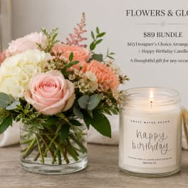 Pink and white flower arrangement in a glass vase beside a lit birthday candle.