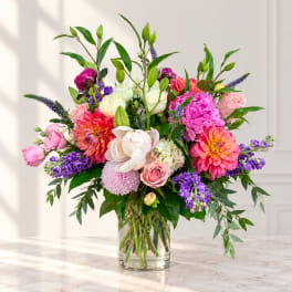 Mixed bouquet of pink, purple, white, and orange flowers in a clear glass vase