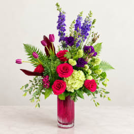 Mixed bouquet of pink roses, purple blooms, and green hydrangea in a tall glass vase