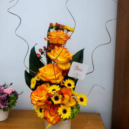 Tall arrangement of orange roses and yellow daisies in a white vase