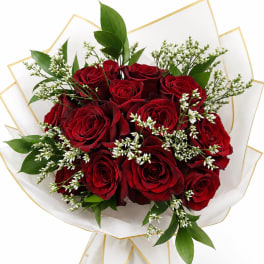 Bouquet of red roses with white filler flowers and green leaves in white wrap