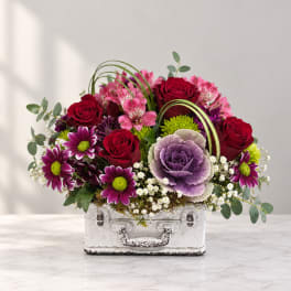 Mixed bouquet in a white suitcase-style container with red roses and purple flowers