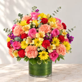 Colorful mixed bouquet in a green glass vase with pink, yellow, red, and peach flowers