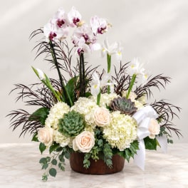 Orchid and rose arrangement in a wooden bowl with a white ribbon