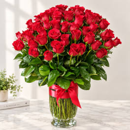 Red roses arranged in a clear glass vase with a red ribbon