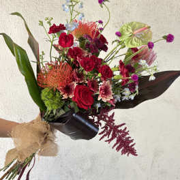 Hand-tied bouquet of red and pink flowers with dark wrap and burlap