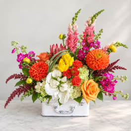 Colorful mixed flower arrangement in a white suitcase-style container