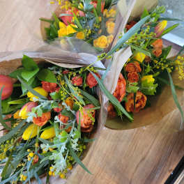 Three wrapped bouquets of orange and yellow tulips with greenery