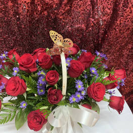 Red roses and purple daisies in a white basket with a butterfly topper
