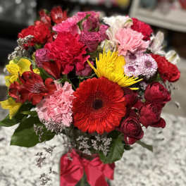 Mixed bouquet of red, pink, and yellow flowers in a glass vase with a red ribbon