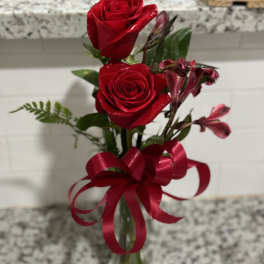 Two red roses with pink alstroemeria in a glass vase tied with a red ribbon.