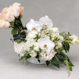 White and blush floral arrangement in a low vase with orchids and roses