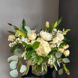 White floral arrangement in a clear glass vase with mixed greenery