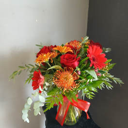 Red and orange mixed bouquet in a glass vase with a red ribbon