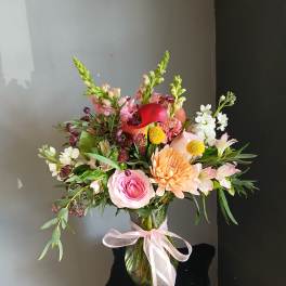 Mixed bouquet of pink, peach, white, and red flowers in a glass vase with ribbon