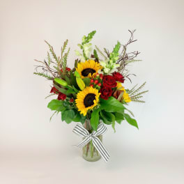 Sunflowers and red roses in a glass vase with a striped ribbon