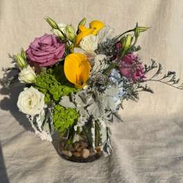 Mixed bouquet in a glass vase with yellow calla lilies, roses, and white blooms
