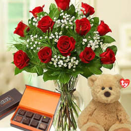 Red roses in a glass vase with a teddy bear and chocolates