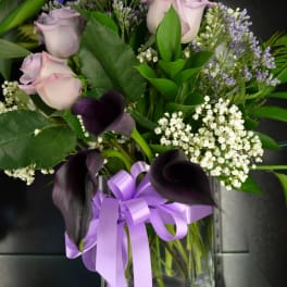 Lavender roses and dark calla lilies in a glass vase with a purple ribbon