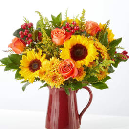 Sunflower and orange rose bouquet in a red pitcher vase