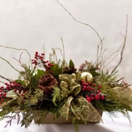 Holiday centerpiece with pinecones, red berries, and a patterned ribbon in a low container