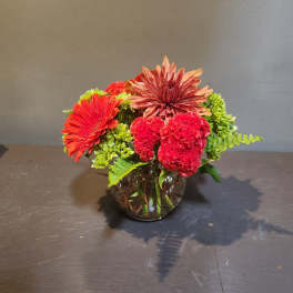 Mixed red and orange flowers in a round glass vase