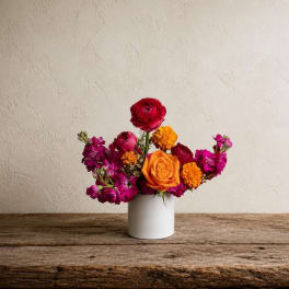Colorful mixed flower arrangement in a white vase on a wooden table