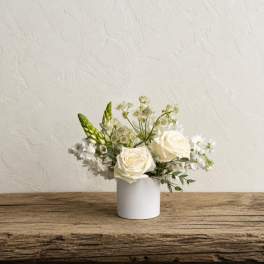 White roses and small white flowers arranged in a white vase