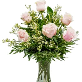 Light pink roses arranged in a clear glass vase with greenery